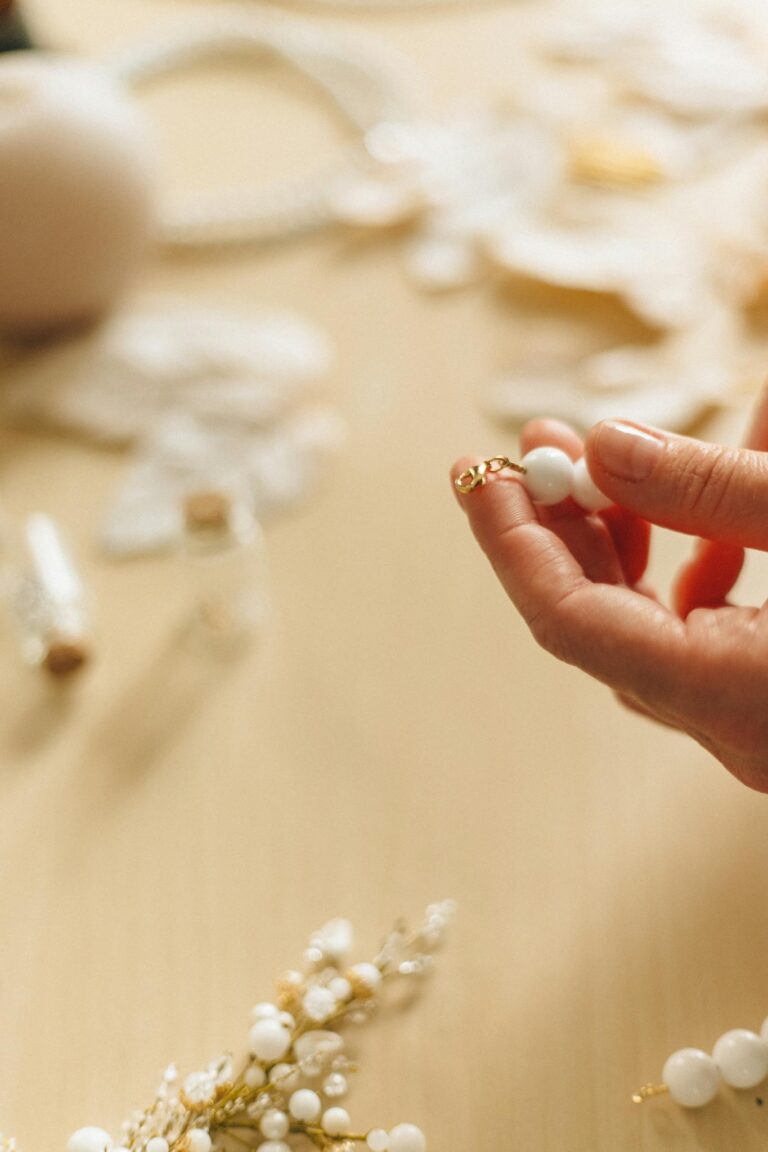 Close-up of hands crafting jewelry with delicate white beads and gold accents.