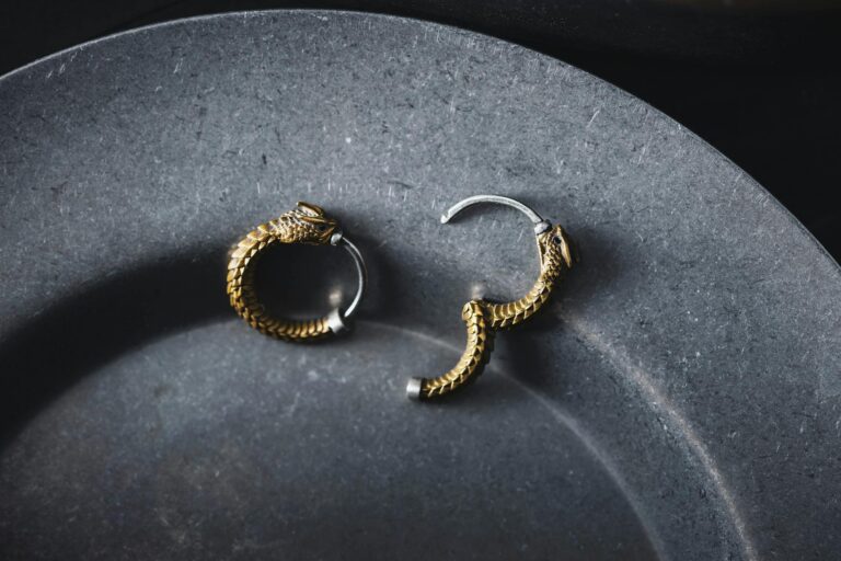 Close-up of intricate gold dragon earrings on a dark slate plate, showcasing luxury jewelry design.